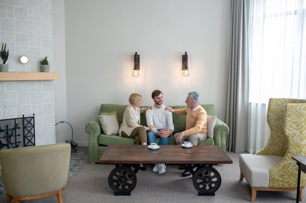 Elderly couple sitting on a sofa and talking warmly with a younger man at home.
