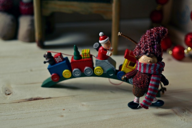 Elfin figurine in a knit hat and scarf standing beside a festive toy train