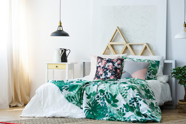 Bright bedroom with white bed, green leafy blanket, floral pillows, pendant lights, and minimal Scandinavian decor.